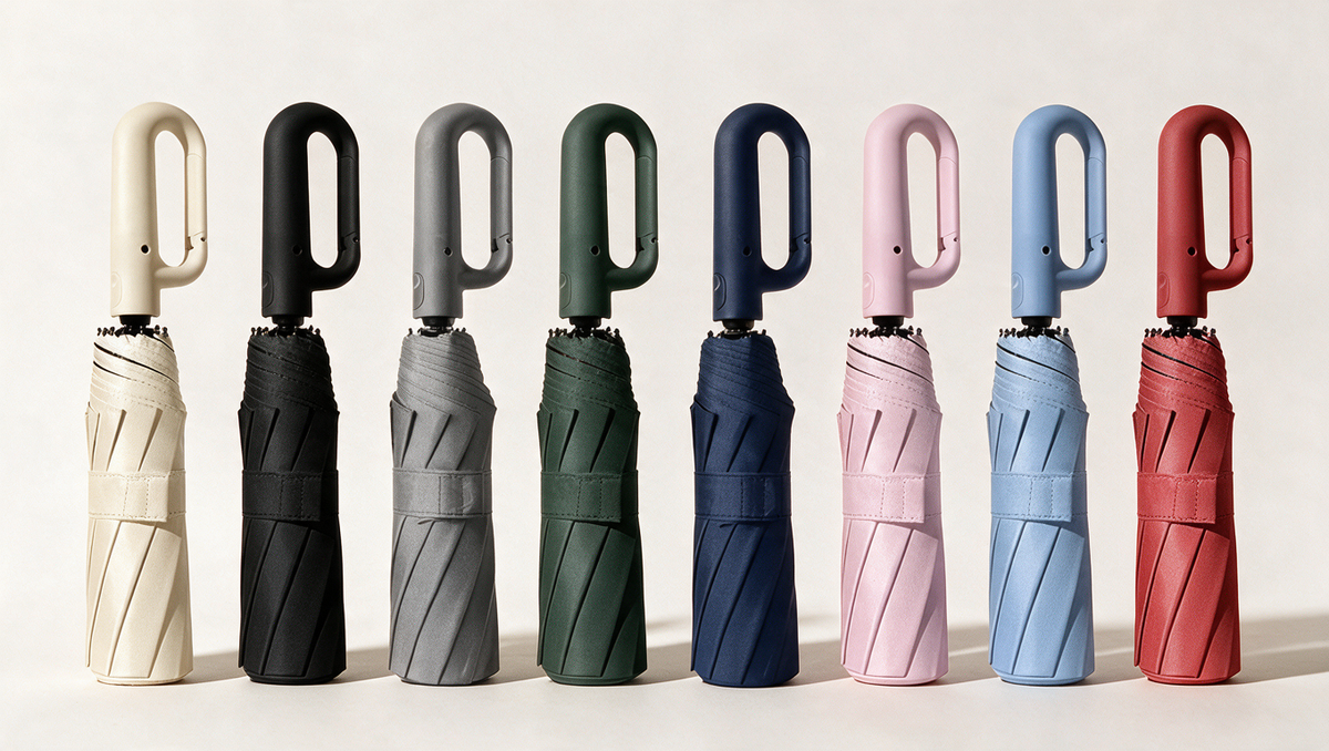Eight Ombriel Loop umbrellas folded in a row: beige, black, grey, forest green, navy, pink, sky blue and burgundy