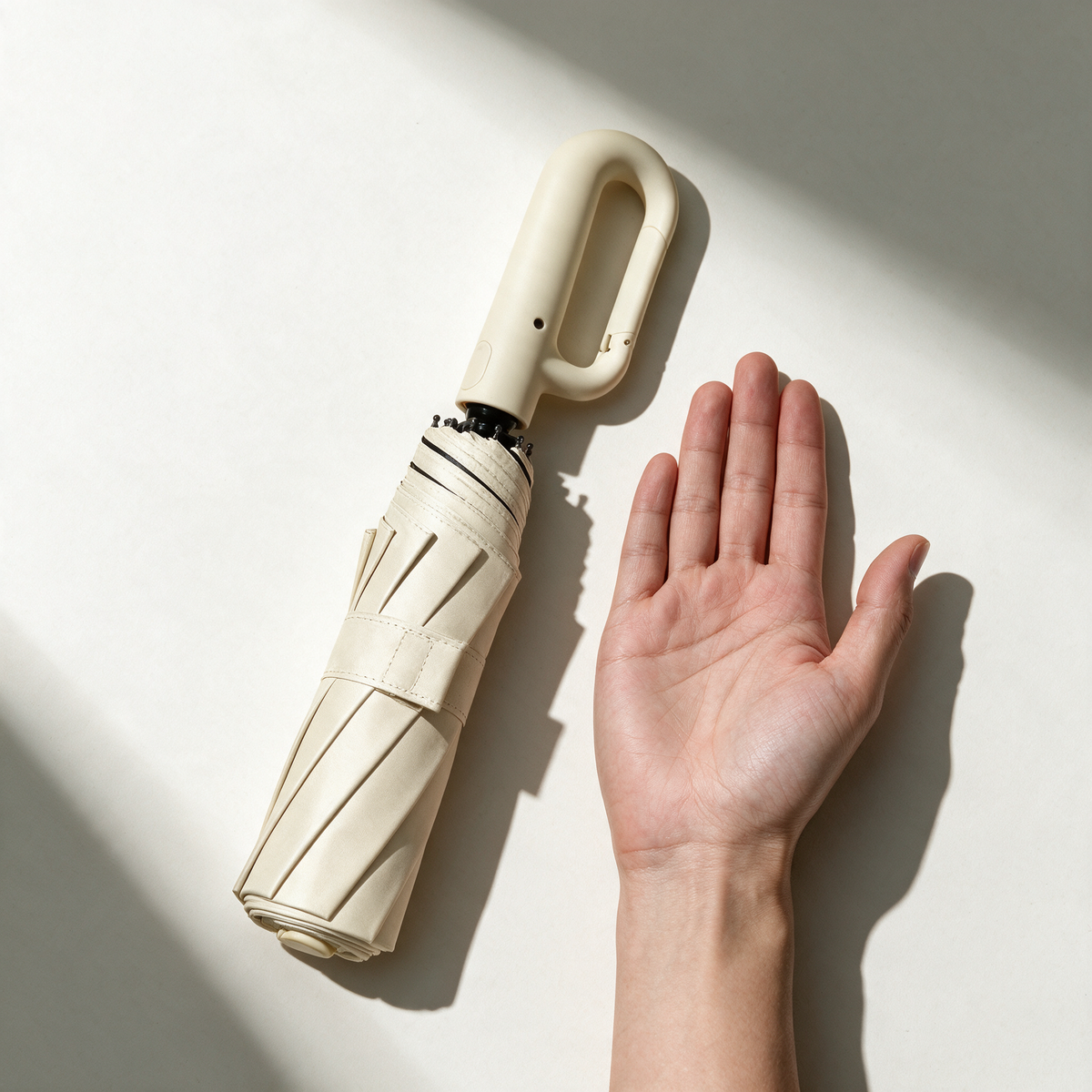 Folded Ombriel Loop umbrella in beige lying next to an open hand for scale, 37 cm long